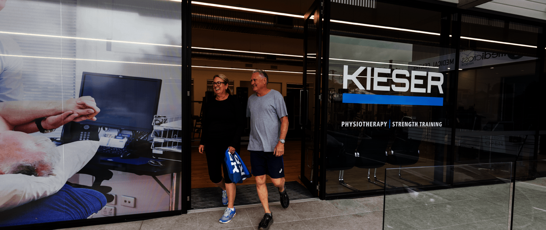 Two smiling people at entrance of a Kieser clinic